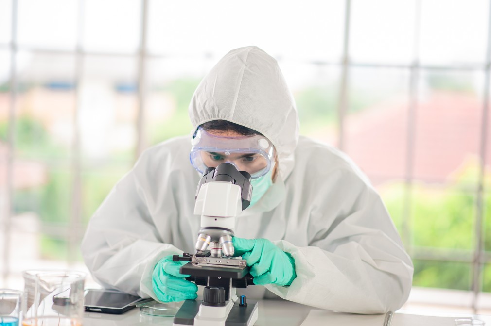 A person wearing full PPE doing research with a microscope