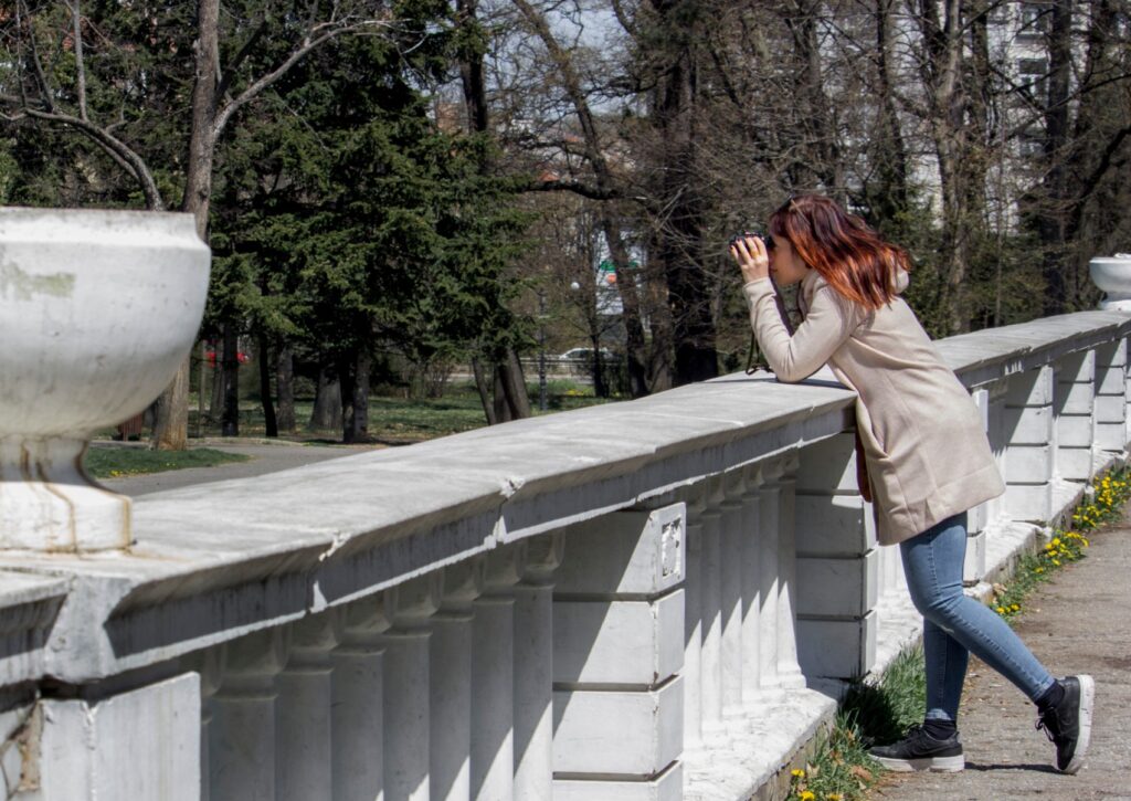 woman looking over a railing outside with binoculars watching something