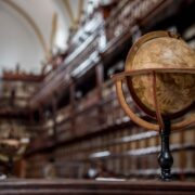 Featured image for Is Dark Academia Still Popular? to illustrate the dark academia aesthetic, it shows a picture of an antique library in the background with an old globe in focus on a table. The picture's vibe is dark and moody.