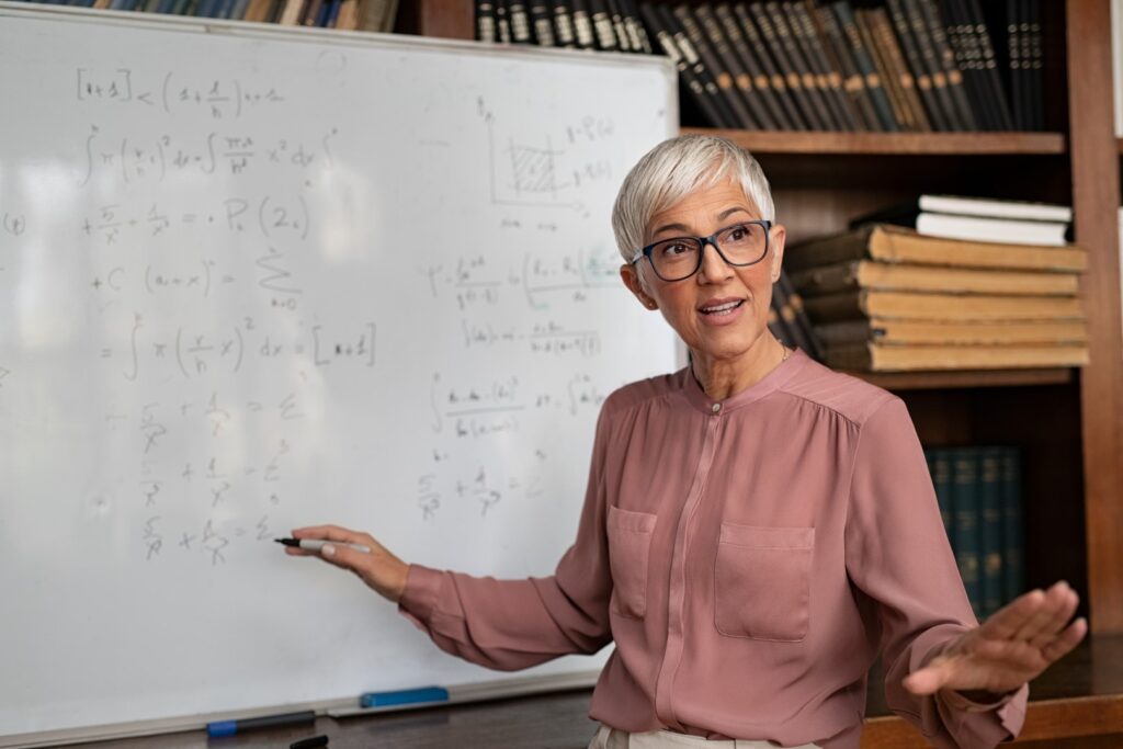 female college professor teaching math in front of a whiteboard to show that academia is good for dark academia inspired jobs